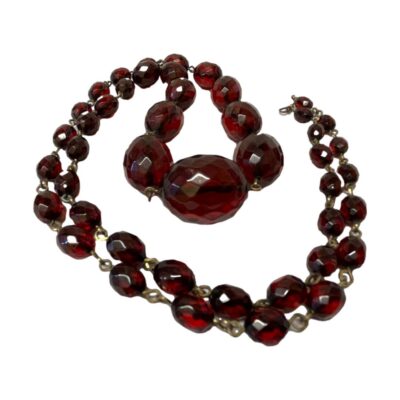 Art Deco cherry bakelite necklace. Lovely Art Deco graduating faceted cherry bakelite necklace with metal links separating each bead. There is no clasp as necklace is long and can fit over the head. The largest bead measures 30mm long and 20mm wide. 60 grams. Photo of necklace displayed on a flat surface and laid out in a swirl pattern.