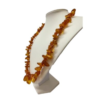 Vintage Baltic amber necklace. Nice length Baltic amber necklace with mostly cognac amber and the occasional butterscotch and egg yolk pieces. Amber screw clasp. The largest piece at the front measures 30mm long. 62gms. Photo of necklace on display stand and seen from a slight side angle. Display stand is facing left.