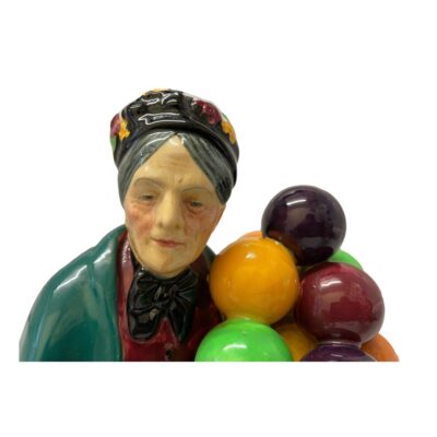 The old balloon seller by Royal Doulton. Bone china figurine of The Old Balloon Seller Number number H.N.1315 In excellent condition with no chips, cracks or crazing. A fine collectors piece. Close up photo of the balloon sellers face with a few balloons on the right. Close up, she has a kindly face.