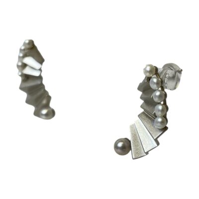 Sterling silver earrings with Madama Akoya pearls. Beautiful fan like sterling silver earrings each set with 5 small pearls at the top outer curve and one larger pearl to the end. The industrial look finish of the silver compliments the pale grey hue of the pearls perfectly. Hallmarked S925 to the back. Drop length approximately 30mm and 10mm at widest. Photo of both earrings displayed on a stand and seen from a slight sideways angle with one slightly in the foreground.