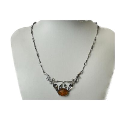 Sterling silver necklace with amber. Art Nouveau style sterling silver necklace with foliate design front with a single piece of amber to finish. Attached fetter and twist chain compliments the look. Hallmarked 925 to the back of amber and to the clasp. Necklace front measures 65mm wide at the top and hangs 45mm long. The amber measures 18mm by 12mm. Main photo of necklace displayed on a stand and seen front facing forward.