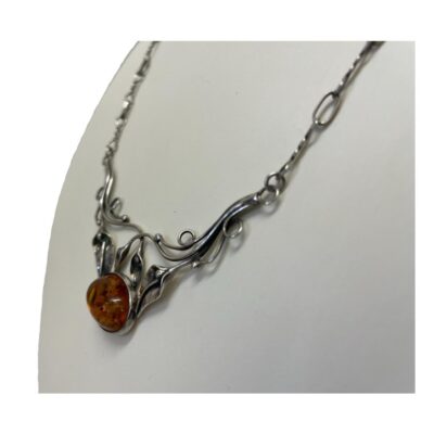 Sterling silver necklace with amber. Art Nouveau style sterling silver necklace with foliate design front with a single piece of amber to finish. Attached fetter and twist chain compliments the look. Hallmarked 925 to the back of amber and to the clasp. Necklace front measures 65mm wide at the top and hangs 45mm long. The amber measures 18mm by 12mm. Photo of necklace on a display stand and seen with amber front facing towards the left.