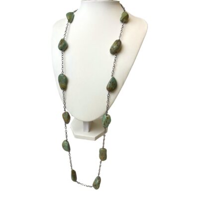 Antique Tibetan turquoise necklace. 19th century necklace with large pieces of Tibetan turquoise stones. Long necklace with large pieces of Tibetan mountain turquoise stones separated with white metal chain. The necklace does not have a clasp so intended for wearing long. The beads average around 30mm long with varying widths. Weighs 96 grams. Photo of necklace on a display stand and seen from a slight side angle towards the left.