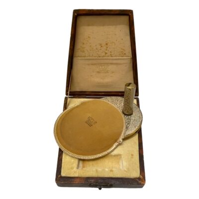 Vintage Vogue compact and lipstick holder set. An original Vogue cased set consisting of a compact with cover and a lipstick holder. Both in a lovely gilt metal with a floral decoration in an off white colour. Both compact and lipstick holder have some contents within. The case is original with signs of wear on the outside, foxing to the lining inside and the top half of clasp is missing. Photo of the compact half inside its cover with lipstick holder standing upright on the protruding compact. All 3 pieces are displayed on the bottom half of the case.