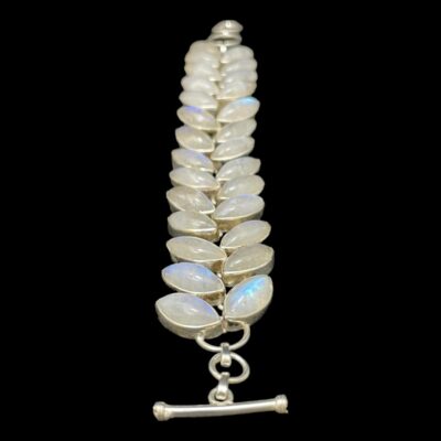 Vintage bracelet set with rainbow moonstones. Sterling silver bracelet set with 27 stunning eye shaped rainbow moonstones. The stones are of high quality that flash colours in different shades of vibrant blues with hints of yellow and green. Slightly adjustable from 155mm to 195mm long. 25mm wide. Hallmarked 925 for sterling silver. Photo of bracelet laid out in a vertical line with the toggle clasp end in the foreground. A few stones have flashes of vibrant blue visible.