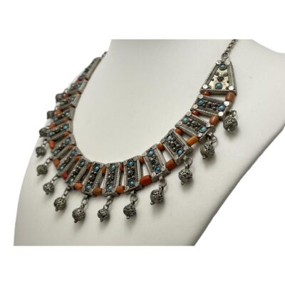 Silver collar necklace marked Ag. Beautiful collar necklace with rectangular silver panels each embellished with 2 small turquoise stones and a small silver filigree ball hanging from the ends. Each panel is separated by 2 coral beads, short to the top and longer at the bottom to create the rigid U shape of the collar. Possibly a bridal piece. Hallmarked Ag to the clasp ring and marked 930 made in Israel to back of one end panel. Measures approximately 400mm long. One panel length with end ball measures approximately 35mm. Photo of collar on a display stand and seen from a slight side angle.
