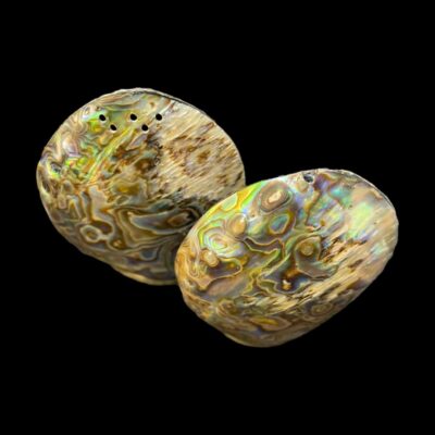 Vintage Asprey & Co Ltd abalone salt and pepper. Beautiful oval shaped abalone salt and pepper pots finished with sterling silver bases. The flat egg shape of these pots make them very easy to hold. Both hallmarked to the base for London assay c1971. Both pots are missing their stoppers. Measurements approximately 52mm at longest in the middle, 15mm at widest and 70mm tall. Photo of the pots seen from a raised angle looking down. The salt pot with one hole is to the foreground to the right and the pepper is behind and to the left.