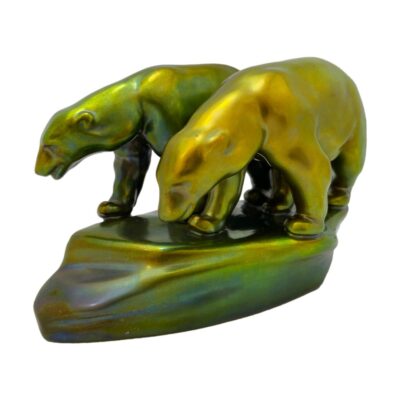 Zsolnay porcelain polar bear ornament. Striking porcelain polar bears in the famous Eosin glaze. This glaze technique was created by Vilmos Szolnay which produces iridescent metallic colours unique to each piece. These polar bears are in iridescent green with hues of gold and blue featuring in the colour play. Stamped to the base. Main photo of the ornament seen from a diagonal angle with the bears heads facing bottom left. The golden yellow bear is in the foreground with the larger greener bear behind. The rock they are standing on is in hues of iridescent green, yellow, blue and brown.