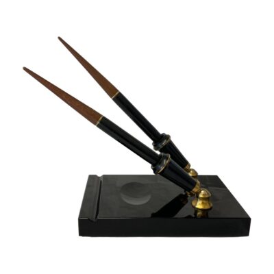 Vintage double desk set by Parker. Very chic desk top double pen set. The set consists of 2 Vacumatic fountain pens, one with 14kt gold fine point nib and other with a gilt metal italic nib. The stand, in smooth black granite like stone has a pen rest and an oval space probably for the ink bottle. The whole set is colour coordinated in black and brass with brown to the pen ends which twist off to reveal the filling mechanism. Each pen measures 210mm long. Pen holder slots are 75mm tall. Stand measures 75mm long, 113mm wide and 22mm. Photo of stand seen from the side. The pens are in their stands and displayed with one at the back posed slightly above the one in foreground.