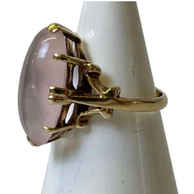 Vintage 9 karat gold ring with rose quartz cabochon. The pale pink of the quartz and gold setting compliment each other beautifully. c1967 Birmingham assayed. Ring size J / 4.75 Ring weight 3.9grams. Photo of ring on a cone shaped display stand and seen with ring front facing left. 3 side prong fixings on the shoulder are clearly shown
