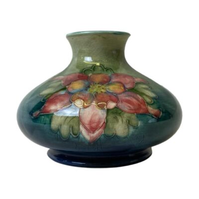 Vintage Moorcroft vase in orchid pattern. Small bulbous Moorcroft vase in sea green/blue with a pink and mauve orchid to either side. Moorcroft stamp to the base. In good condition with only minimal crazing. c1940s. Measures 68mm in diameter at base, 105mm at widest and 40mm across the top. Main photo of vase from an eye level and showing the side with the pink orchid.