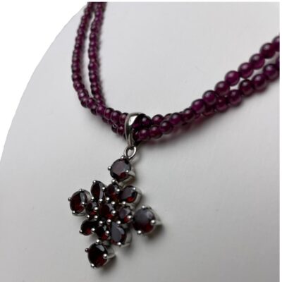 Garnet necklace and pendant in silver. Lovely 2 strand garnet bead necklace with silver clasp and a sterling silver and garnet pendant. The garnet beads on the necklace are almadine in a pink/purple shade and the 4 pointed star shaped pendant has wine red colour garnets. The pendant can be removed if desired. Necklace is slightly adjustable from 450mm to 500mm. Pendant drop length 40mm and width 30mm. Photo of necklace on a display stand and seen from a slight sideways angle with the pendant front facing left.