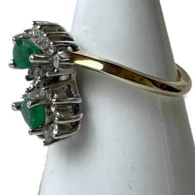Vintage ring with emeralds and diamonds. Pretty ring set with 2 pear shaped emeralds each surrounded by 12 brilliant round cut diamonds in a 9 karat white gold cluster setting and a 9 karat gold shank. Ring size N / 7.5. Weight 4.2 grams. Photo of ring displayed on a cone shaped stand with the ring front facing left.
