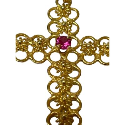 18 karat gold cross with ruby. Very pretty petite 18 karat gold cross with a round cut ruby to the centre. Lovely detail to the gold cross which is made up entirely of tiny circles and decorated down the middle of each arm with gold flowers. Hallmarked 18kt to the bail. Drop length from bail 30mm. Close up of the central area of the cross with focus on the ruby.
