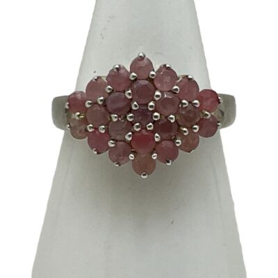 Sterling silver ruby cluster ring. Pretty pink ruby cluster ring set on sterling silver. Total of 23 small round cut pink rubies are set in a diamond shape and each stone separated with silver rod dividers. Ring size O.5 / 7.25. Main photo of ring displayed on a cone shaped stand and seen with ring front forward facing. The cluster of rubies is set with 5 in a vertical row to the centre, 4 either side of this then 3 then 2 at the ends.
