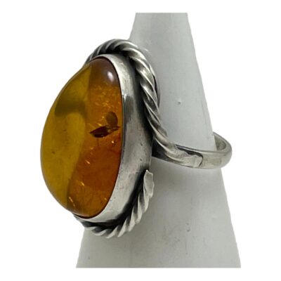 Vintage sterling silver ring with amber. Large statement ring with cognac amber set in sterling silver. Nice rope twist silver design starting at each shoulder and worked around the stone to top and bottom. Hallmark to the outside of band at back. Ring size N.5 / 7. Photo of ring on a cone shaped stand and seen with ring front facing left.