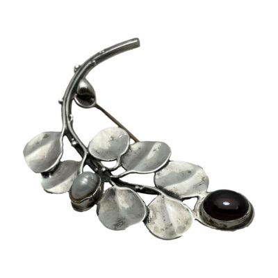 Art Nouveau sterling silver branch brooch. Pretty brooch in the form of a branch with leaves and a single deep red garnet cabochon at the tip and a freshwater pearl mid way. Hallmarked 925 to the back of the brooch on stem. Photo of brooch seen with the garnet tip end in the bottom right foreground. The curve of the branch is seen displayed like the letter C.