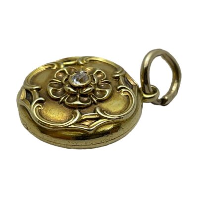 Gold locket with old cut diamond. Very pretty round locket in unmarked yellow gold decorated to the front with a Tudor Rose style design and an old cut diamond to the centre. The original glass remains inside which appears to be completely stuck and may need professional intervention to remove. Drop length from top of bail 2.8mm. Locket weight 7 grams. Photo of locket shown face up and laid sideways with the bail end to the right
