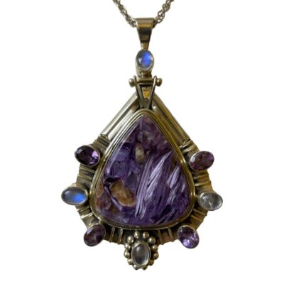 Statement charoite pendant on silver chain. Large striking sterling silver pendant with a substantial charoite stone to the centre and amethyst & rainbow moonstones evenly distributed around it and set in sterling silver. A rainbow moonstone also adorns the unusual bail. Hallmarked 925 to back of pendant and clasp. Pendant measures 88mm long from top of bail and 55mm at widest. Close up photo of the pendant area only with the rainbow moonstones flashing beautiful blue colour.