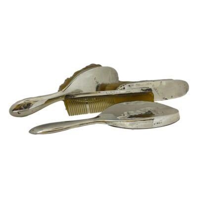 Antique sterling silver dressing table vanity set. c1923 Birmingham assayed sterling set comprising of a hand mirror, hairbrush, clothes brush and comb. All pieces in fair condition with minor dinks except for the clothes brush which has more dinks than others. The comb is missing a tooth and the silver backed mirror has some minor foxing nearer the handle. All pieces have been personalised to Kathleen. Comb measures 185mm by 40mm. Clothes brush is 200mm long at bristles, 40mm wide & 45mm deep. The hairbrush is 245mm long, 65mm at widest, 47mm deep. The mirror is 250mm long, 105mm wide and 16mm deep. Total weight is approximately 20ounces. Main photo of all 4 pieces displayed together. The handles of the hairbrush and mirror are on the left. The mirror is face down in the foreground with comb behind propped up against the back of the clothes brush and the hairbrush on its side in the background.