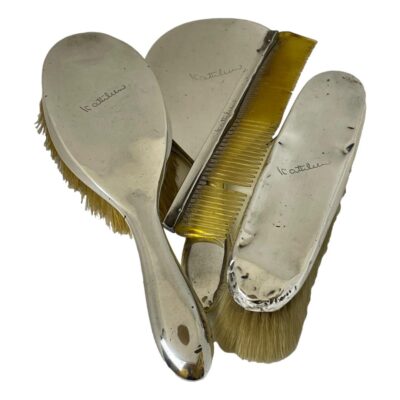 Antique sterling silver dressing table vanity set. c1923 Birmingham assayed sterling set comprising of a hand mirror, hairbrush, clothes brush and comb. All pieces in fair condition with minor dinks except for the clothes brush which has more dinks than others. The comb is missing a tooth and the silver backed mirror has some minor foxing nearer the handle. All pieces have been personalised to Kathleen. Comb measures 185mm by 40mm. Clothes brush is 200mm long at bristles, 40mm wide & 45mm deep. The hairbrush is 245mm long, 65mm at widest, 47mm deep. The mirror is 250mm long, 105mm wide and 16mm deep. Total weight is approximately 20ounces. Photo of all 4 pieces bunched together. Hairbrush on the left, mirror in the middle with comb diagonally laid across the back and clothes brush on the right. All pieces except the comb are face down.
