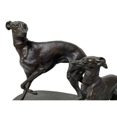 Signed bronze of greyhounds by Mene. A wonderful bronze of an adult & juvenile greyhound in a playful pose. Signed Mene to the top of the base. Measurements 205mm longest, 110 widest and 145mm tallest. Weight 1560 grams. Collect from store only. Close up photo of the front ends of the dogs. The adult is in the background and ahead of the pup. There is a good view of the expressions on both dogs visible.