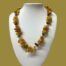 Main photo showing necklace displayed on a stand and seen looking straight on from the front. The necklace is generous in length and hangs below the collar bone. The background colour is a dark mustard which enhances the colours of the amber pieces.