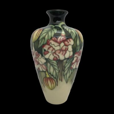 Small Moorcroft vase in fuchsia pattern. Beautiful small vase by Kerry Goodwin for Moorcroft in fuchsia pattern c2001. There are 3 hairline under glaze lines running from the bottom up. Measures 40mm in diameter at base, 85mm in diameter at widest area and 35mm at the mouth. Main photo of vase seen from an eye level and set against a black background. The black enhances the colours of the vase.