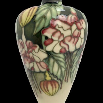 Close up photo of the fuchsia decoration with the flowers in red, pink and cream, the buds have an orange tinge and foliage of light and dark green surrounding the flowers. The lower part of the vase is plain cream coloured.