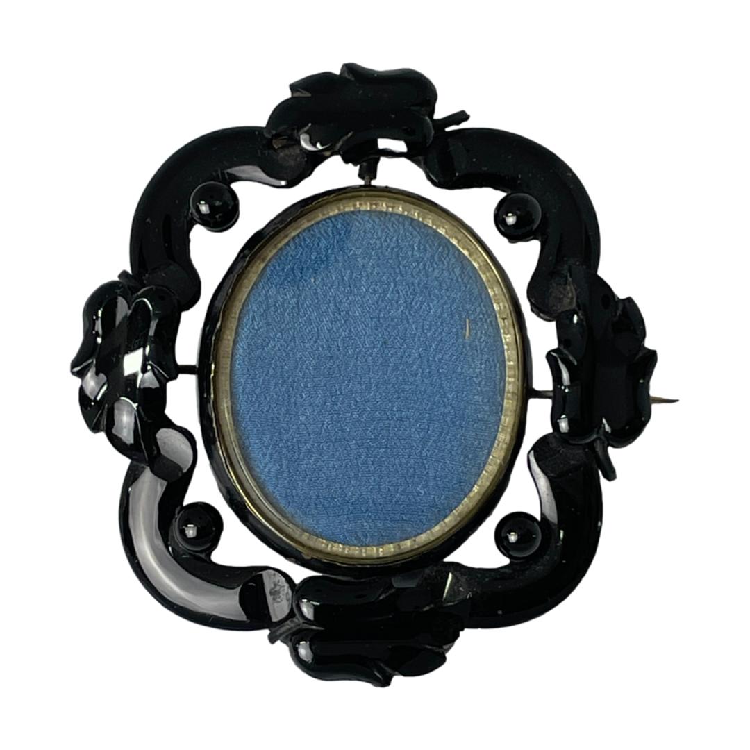 Main photo of locket seen with the pin side to the back. The Whitby jet is carved into an intricate frame with the swivel locket set on a pin at the top and bottom. The locket can only swivel when the pin is opened so the pin side picture is the one closest to the heart!