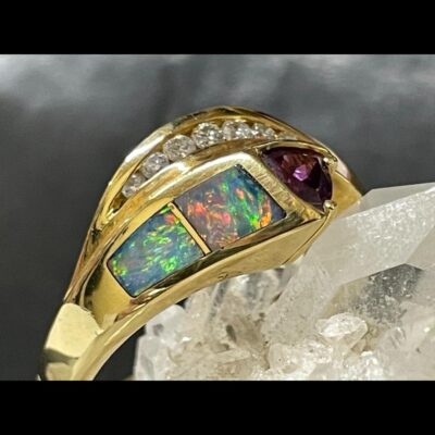 Close up photo of the ring on top of the quartz crystal cluster with focus on the opals and their beautiful colours