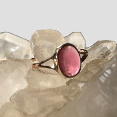 Main photo of ring displayed on top of a cluster of quartz crystal. The ring is facing a little to the right with the light shining through showing the beautiful pink shade of the tourmaline.