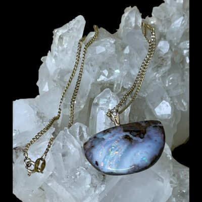 Main photo of the pendant and chain displayed on top of a cluster of quartz crystal. The semi circle pendant has a flattened top with the semi circle forming below. The boulder opal on top of the crystal pushes forth the fact that it is a natural product as do the diamonds. Part of the chain is also visible. The opal being a boulder opal does not have flashes of colour throughout but the majority of the pendant has opal with vibrant colours with a few flecks of dark boulder.