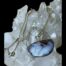 Main photo of the pendant and chain displayed on top of a cluster of quartz crystal. The semi circle pendant has a flattened top with the semi circle forming below. The boulder opal on top of the crystal pushes forth the fact that it is a natural product as do the diamonds. Part of the chain is also visible. The opal being a boulder opal does not have flashes of colour throughout but the majority of the pendant has opal with vibrant colours with a few flecks of dark boulder.