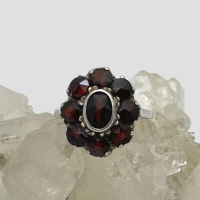 Main photo of ring displayed on a cluster of quartz crystal and shown with ring front forward facing. The garnets are a beautiful deep red colour which is enhanced against the quartz crystal and pale grey background.
