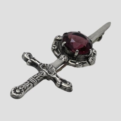 Photo of brooch on a flat surface and angled diagonally with the hilt in the left foreground and the tip of the sword in the top right. The decorative detail to the silver is shown