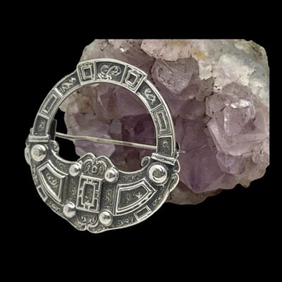 Photo of brooch displayed leaning against a piece of amethyst stone and shown slightly from the side with brooch front facing towards the left.