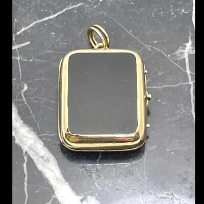 Main photo of locket displayed on top of some black marble with white line inclusions. The bail is to the top and the opening side is on the right. This locket can be worn with either the black onyx or bloodstone side on show.