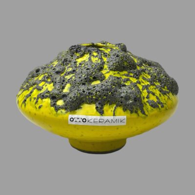 Main photo of vase seen from an almost eye level showing the side with the original Otto Keramik sticker. The vase is a bright lemon yellow base with grey/black lava applied to the top half of the UFO.