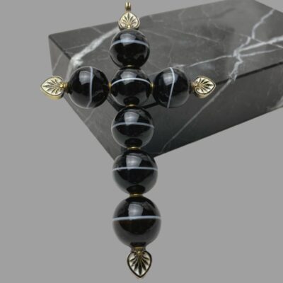Main photo of cross leaning left vertically upright against a block of black marble. The 5 vertical agate beads have the white line going across horizontally whilst the 2 beads making the cross piece show the white band vertically.