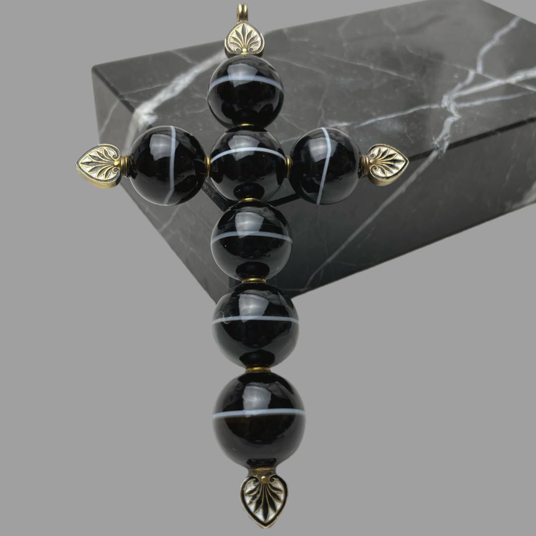 Main photo of cross leaning left vertically upright against a block of black marble. The 5 vertical agate beads have the white line going across horizontally whilst the 2 beads making the cross piece show the white band vertically.