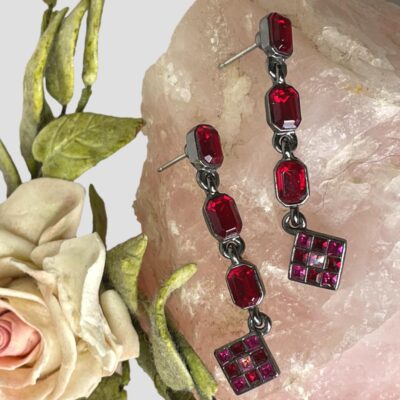 Main photo of earrings displayed on top of some rose quartz with a pale pink rose to its left. The rose quartz shows off the beautiful red and cerise of the crystals in the earrings.