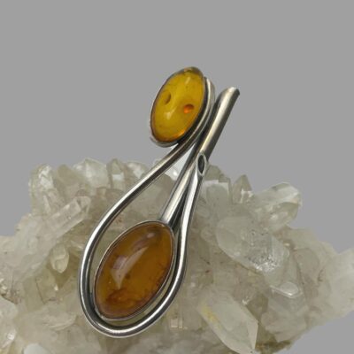 Main photo of brooch displayed against a cluster of quartz crystal. The larger of the amber cabochons is in the lower central part of photo with the smaller cabochon to the top.
