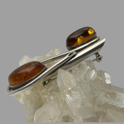 Photo of the brooch displayed on top of a cluster of quartz crystal and seen from a side angle.