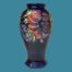 Main photo of vase seen from an eye level with a mauve anemone on display with part of the unopened small blue one to its left. Vase is set against a light air force blue colour which compliments & hi-lights the colours of the vase.