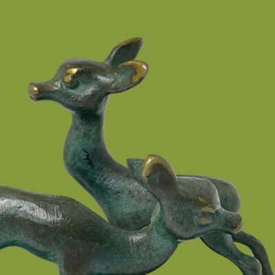 Close up photo of the heads of the deer. The taller one is in the background facing left and shorter one is in the foreground facing right. Nice patina on the metal.
