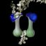 Main photo of the 2 vases shown side by side against a black background to hi-light their beautiful colours. The lower area is green rising to a twisting pattern with white glass and finished with a vibrant blue top. There is a spray of small white orchids in the vase on the left and also between the 2 vases.