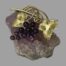 Main photo of the brooch on top of a small rock of natural amethyst. The photo is taken looking straight down at the brooch from above. The grapes are to the centre with a gilt vine leaf to either side. The amethyst stones making the grapes on the brooch are a dark purple in contract to the lilac of the rock. The gilt on the metal is in excellent condition and compliments the purple amethyst beautifully.