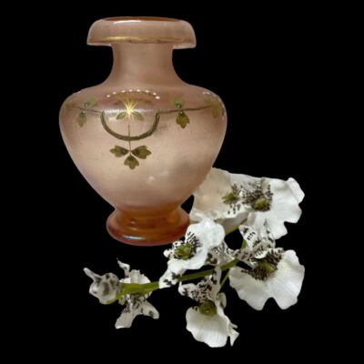 Main photo of vase displayed against a black background with a sprig of white orchid laid along its right hand side. The decorative side on display is the upright flower seen from a cross section angle. The pink is very striking against the black background and the white orchids enhance the white jewel dots on the vase.