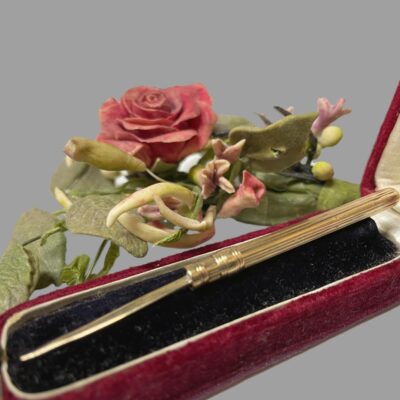Main photo of toothpick displayed fully extended and in the box. The box is a deep red velvet with a raised black velvet interior. The toothpick is fully extended and pick end is to the left.